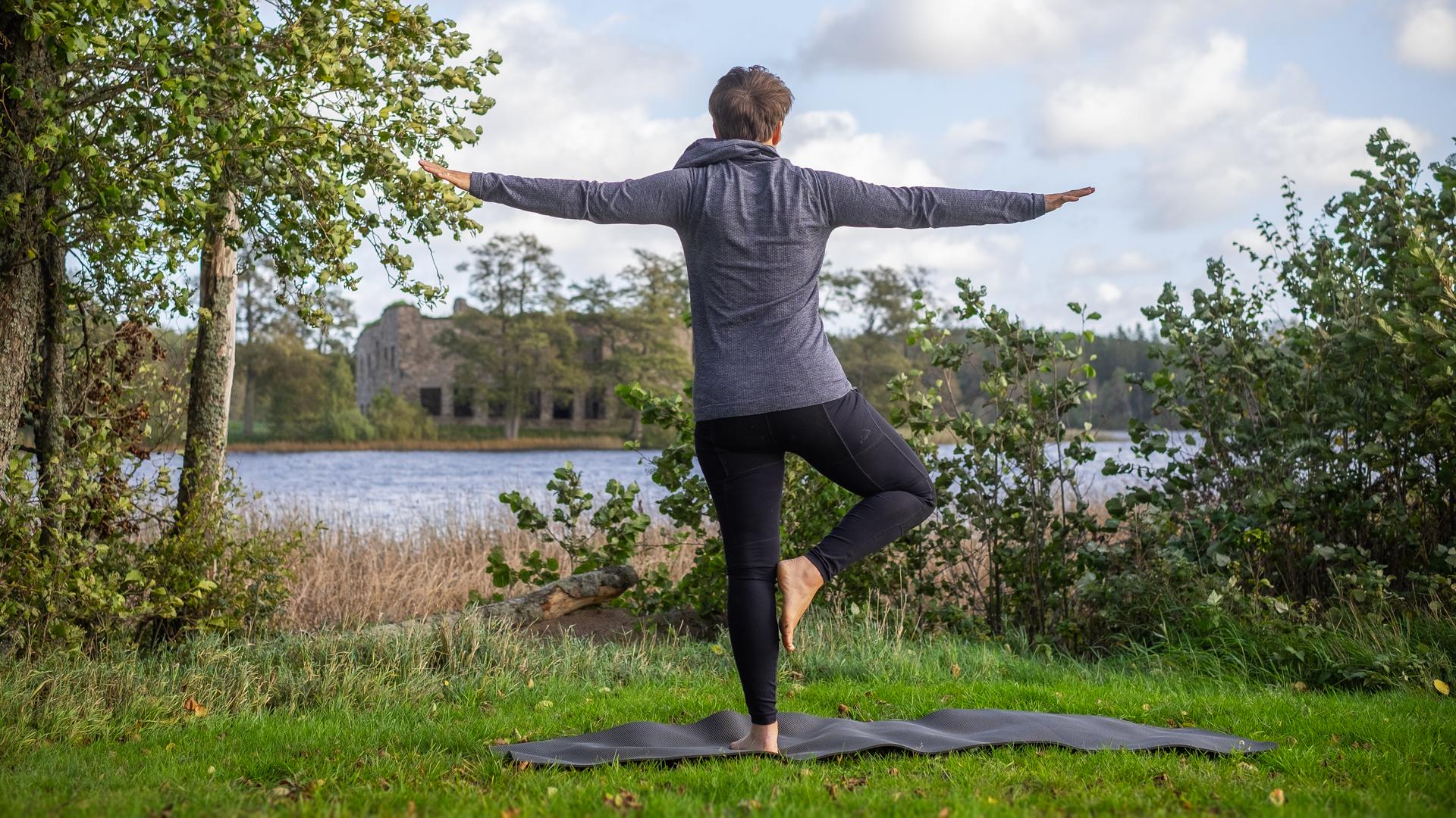 Kvinna i träningskläder gör yogaövning vid en sjö.