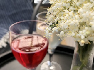 Två vinglas och blommor på ett brickbord ute på en altan. 